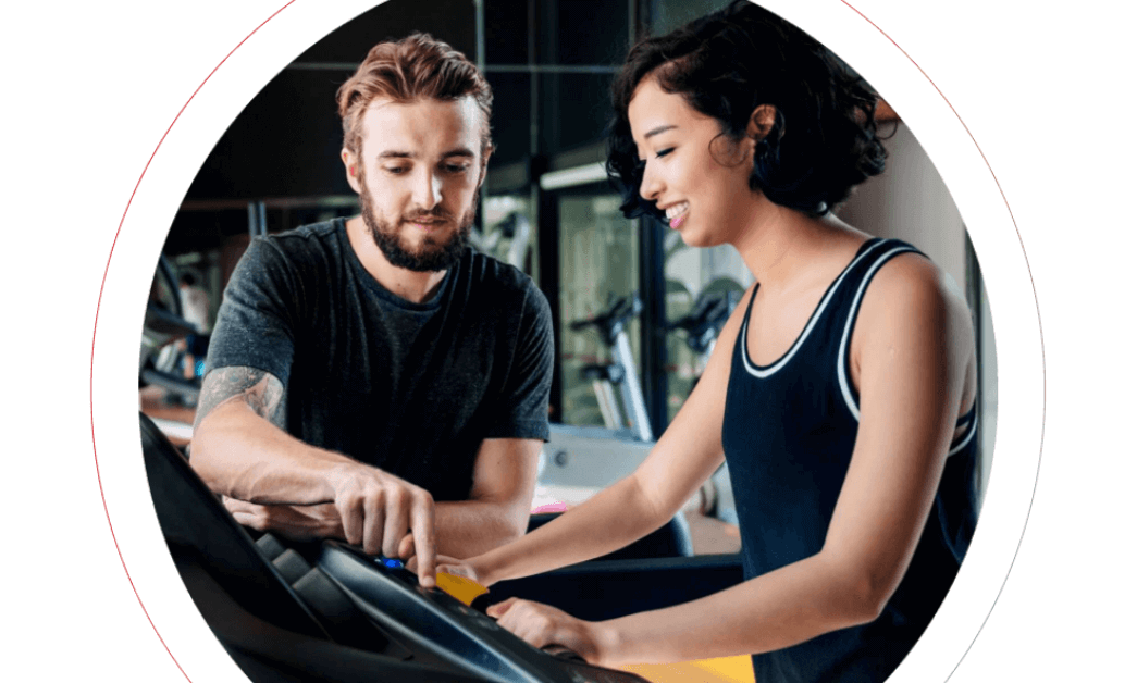 A man and a woman discussing treadmill settings in a gym