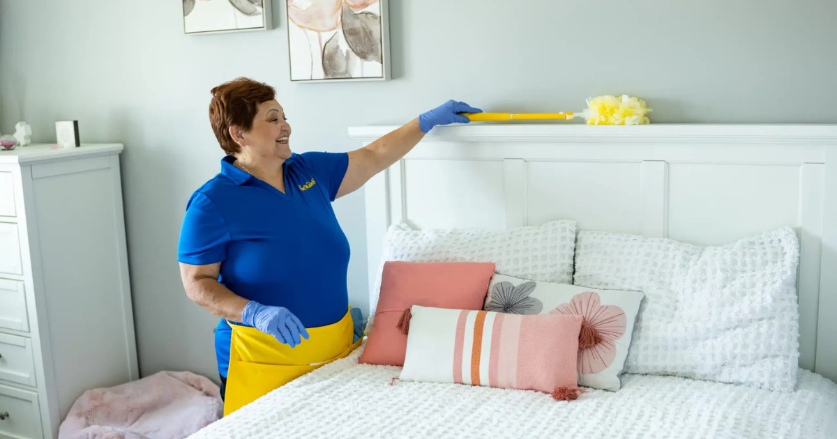 Smiling maid cleaning a modern room with a feather duster in her hand