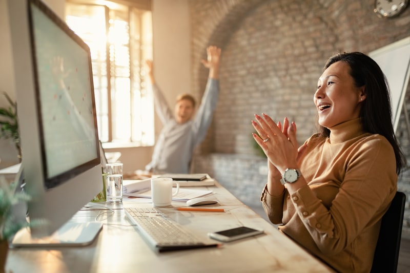 A pair of coworkers in front of a computer, celebrating the results of automation for their Franchise System.