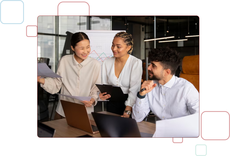 Smiling female customer service representative wearing a headset, pointing at a computer screen while working in an office alongside colleagues.